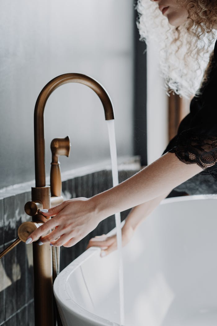 Elegant bathroom scene with a focus on gold faucet and female hands adjusting water flow.