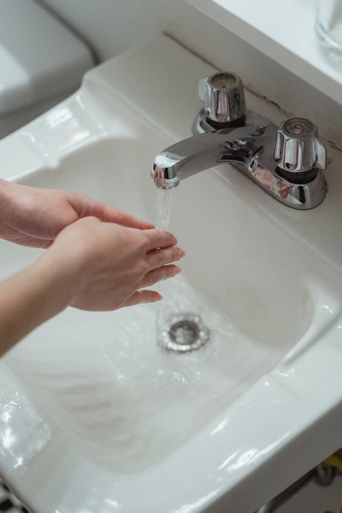Close-up of hands being washed under a modern stainless steel faucet in a white washbasin.